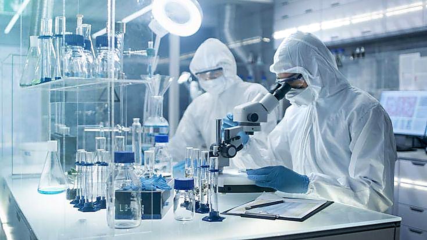Two researchers in protective suits examining laboratory samples with a microscope